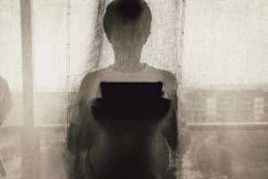 Man Standing Holding A Tablet Behind Curtain